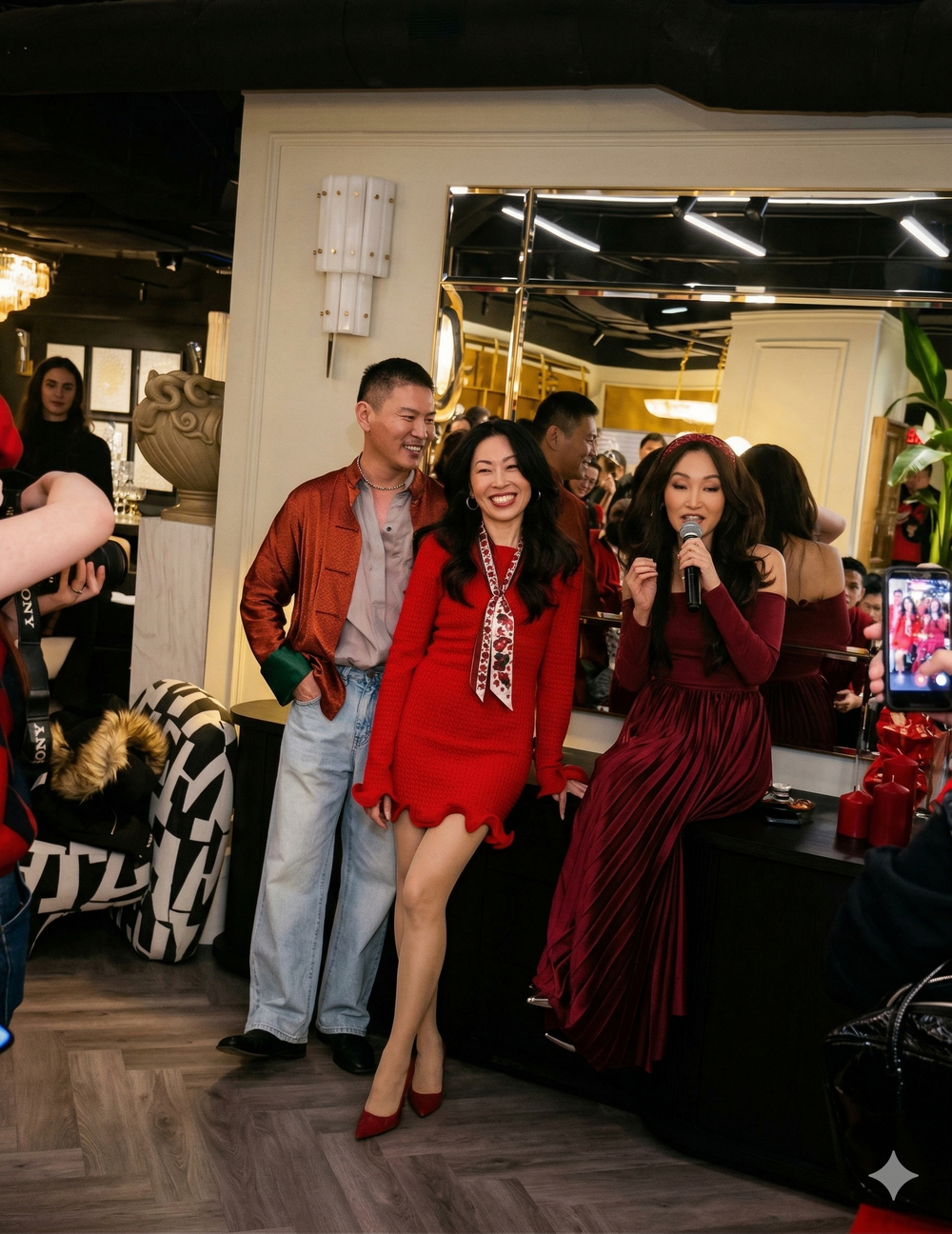Two women in red dresses standing next to a man in a red jacket in a room with mirrors and decor.